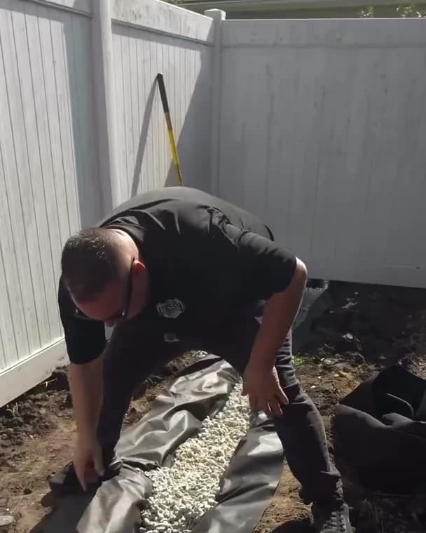 Clean washed gravel inside a TERRA geotextile lined French drain trench along a fence