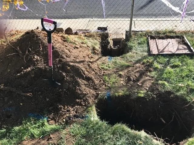 Freshly dug hole with lifted soil piled beside it and a D-handle Spear Head Spade standing in the pile