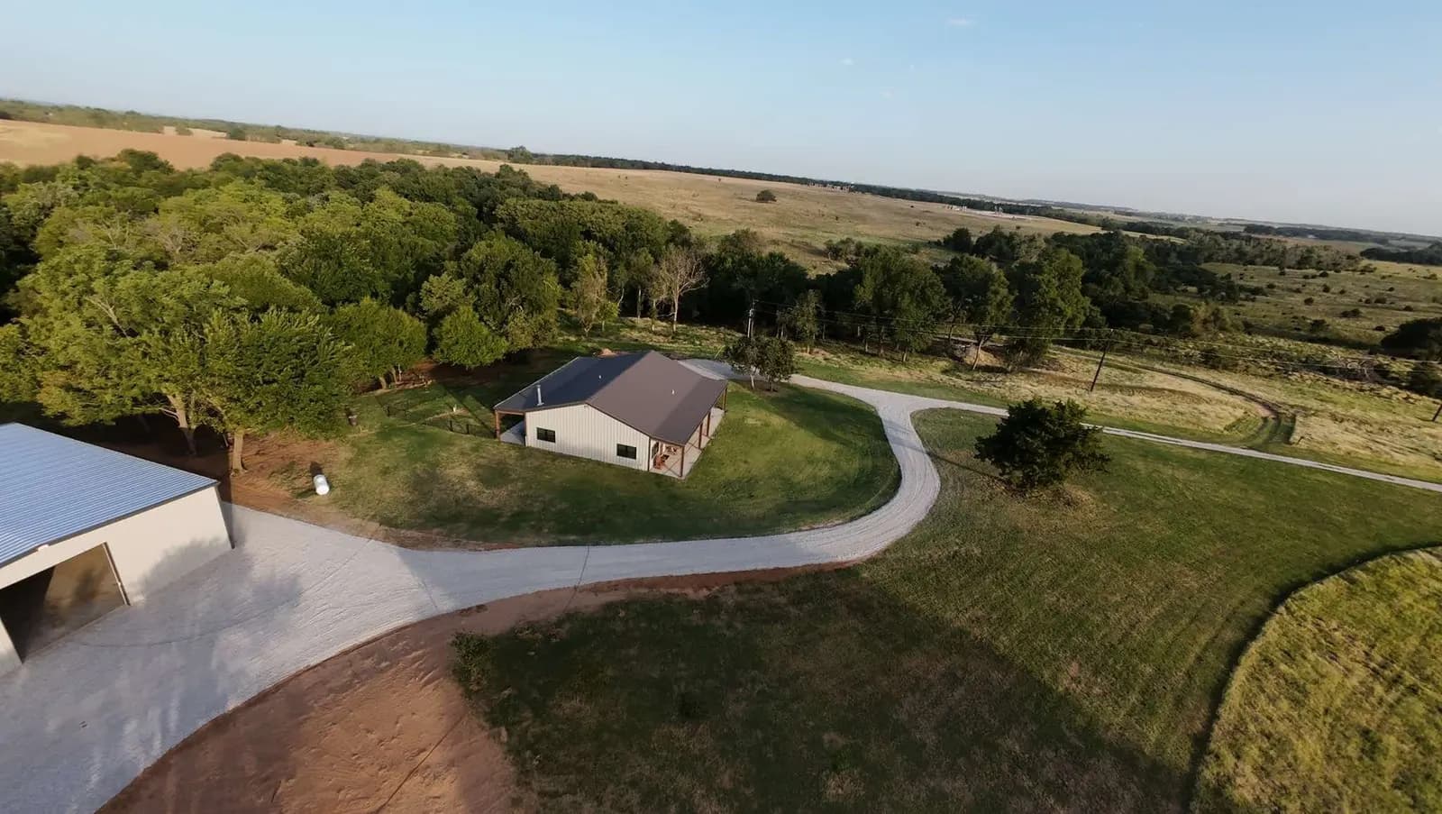 Drone view of a finished gravel driveway curving from a metal shop to a house in Oklahoma, built over DOTDAY XBAR by Okie Hauling