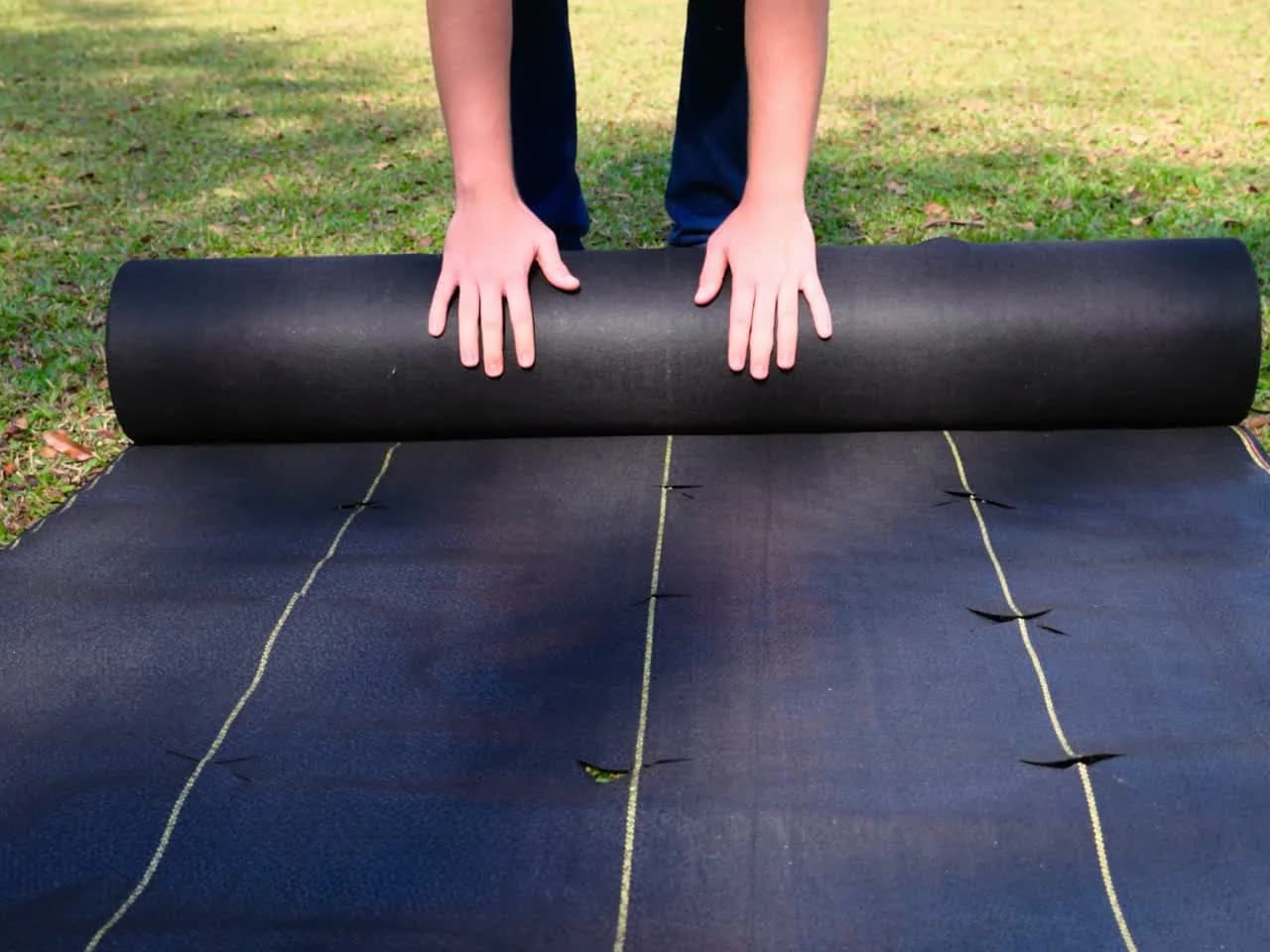 Hands unrolling DOTDAY XBAR fabric across a lawn