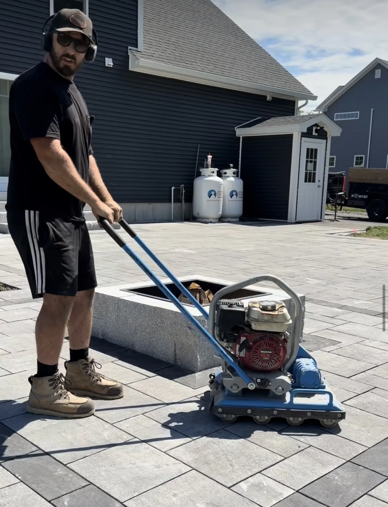 Jeff St Pierre running a plate compactor across a finished paver patio