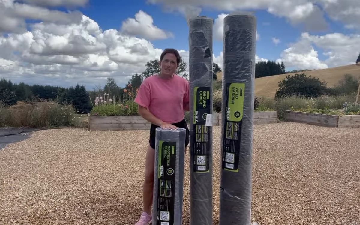 Grower holding the three DOTDAY rolls: TERRA, SHIELD, and XBAR, in a raised-bed garden