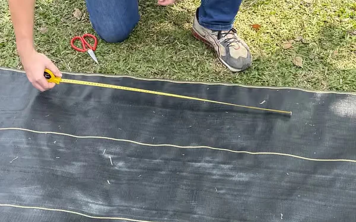 Measuring a run of DOTDAY weed barrier with a tape measure and scissors before cutting