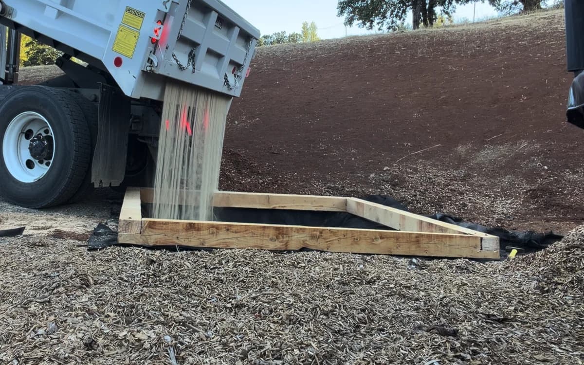 Dump truck filling a timber-framed pad lined with TERRA non-woven geotextile
