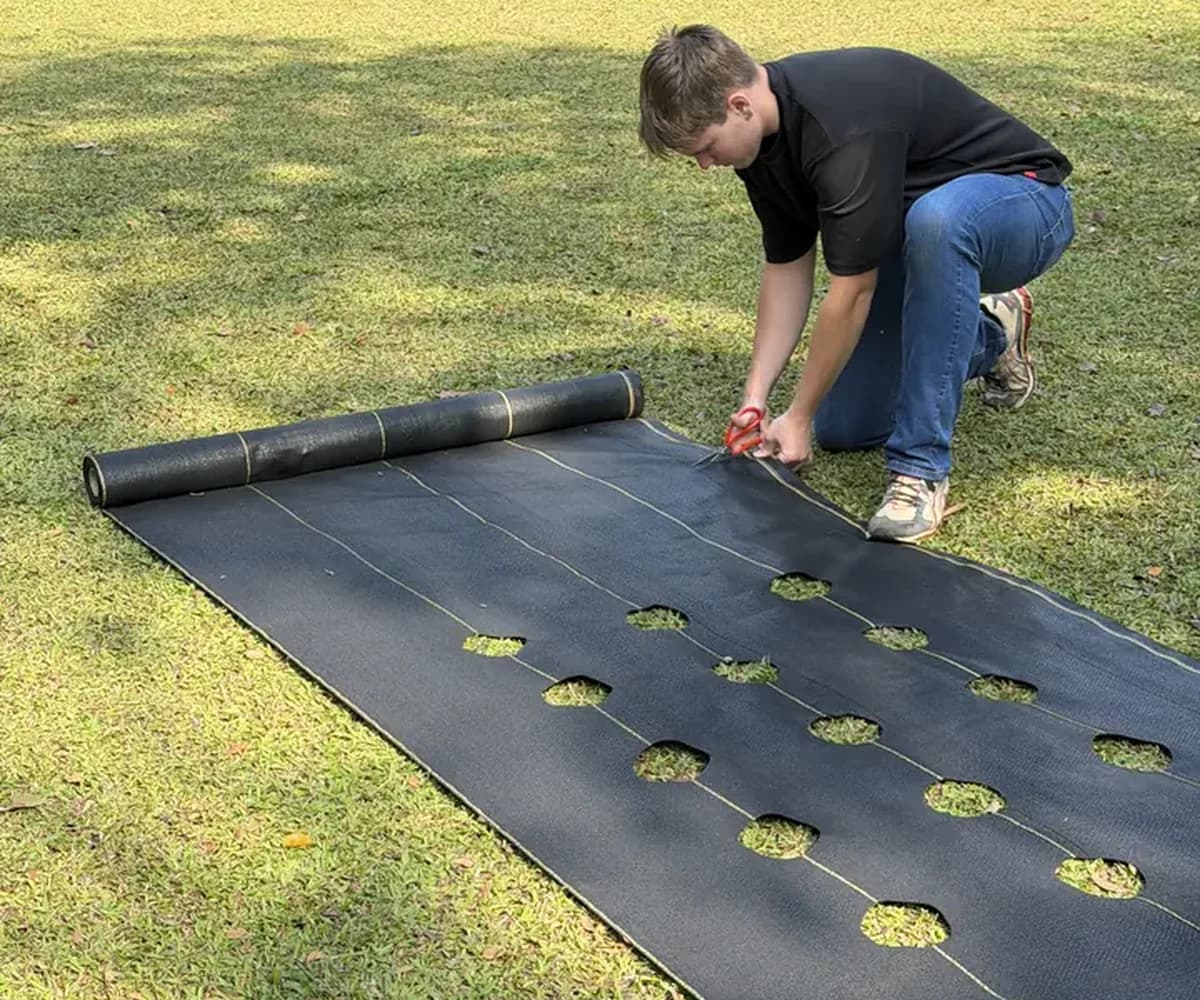 Installer rolling out and cutting DOTDAY landscape fabric on a prepared base before adding gravel