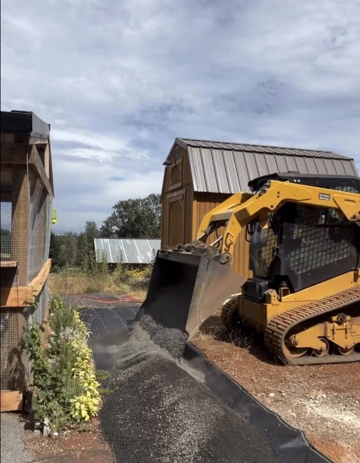 Skid-steer pouring gravel directly onto DOTDAY XBAR landscape fabric on a driveway jobsite