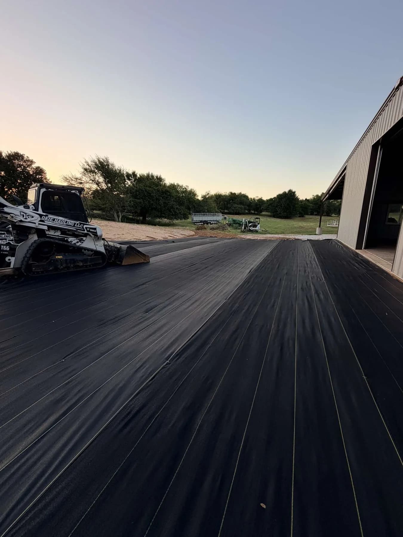 Okie Hauling Bobcat on the far edge of the XBAR covered shop pad at dusk with the shop on the right