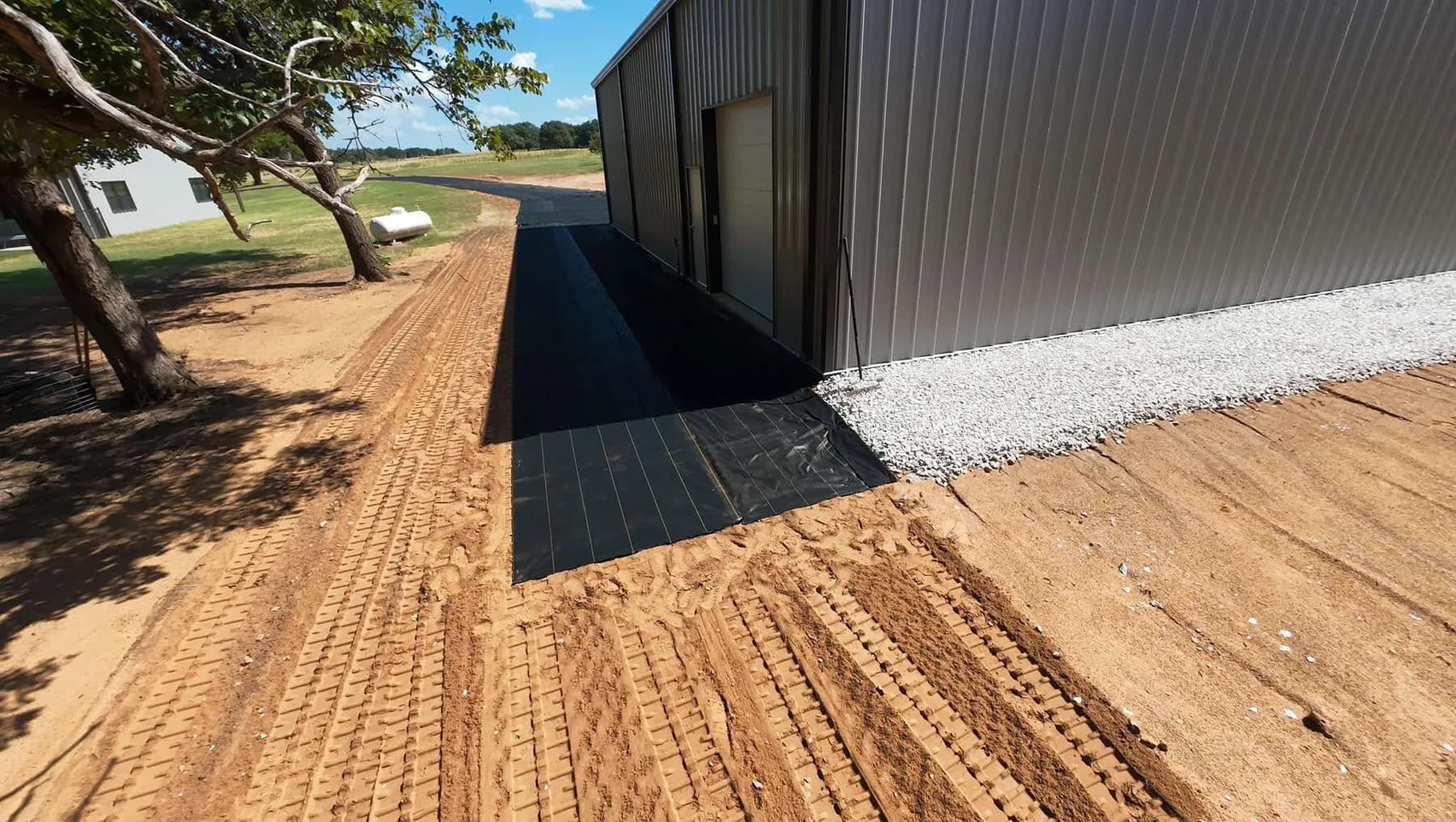 Wide view of XBAR fabric turning the corner of the shop onto the graded driveway with white rock along the wall