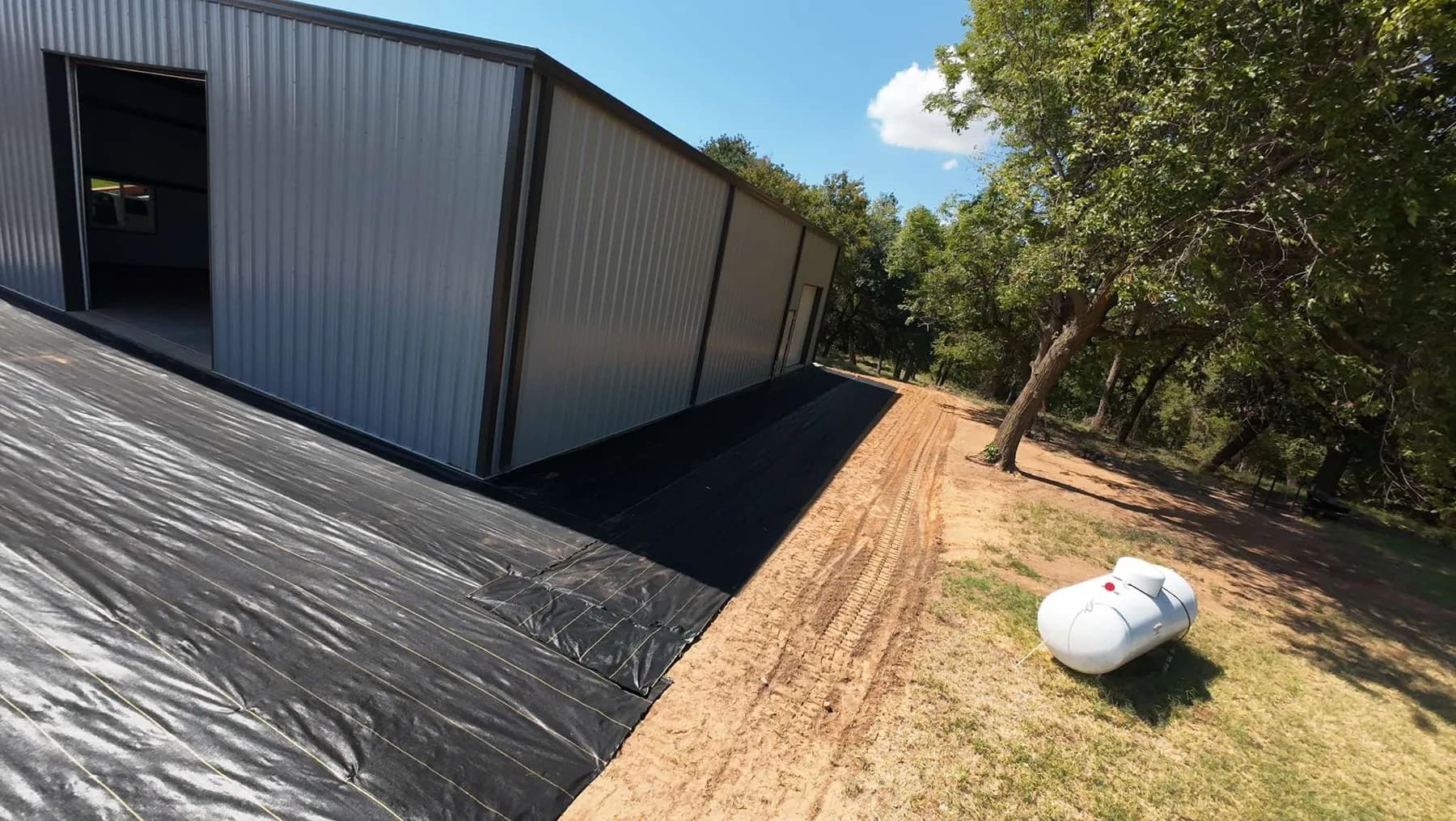 XBAR fabric wrapping the shop corner with the graded driveway and a propane tank on the lawn