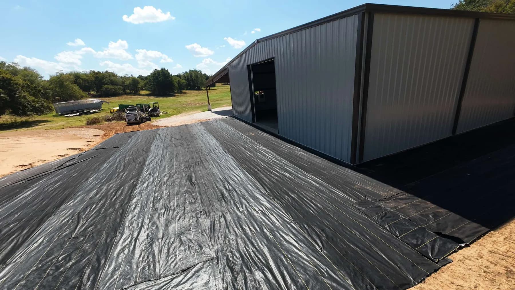 Woven geotextile fabric: DOTDAY XBAR 5oz dual-layer laid across a driveway and shop pad before crushed rock goes down