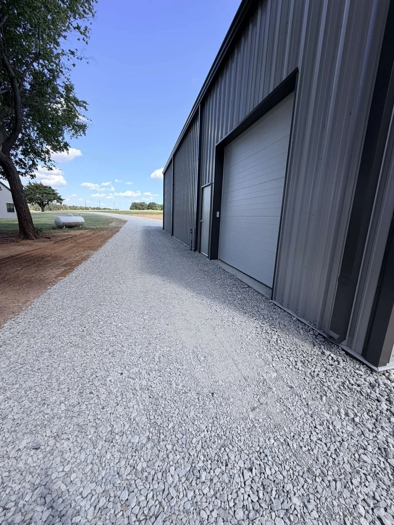 Finished grey crushed rock driveway running past the shop's roll-up door toward the house