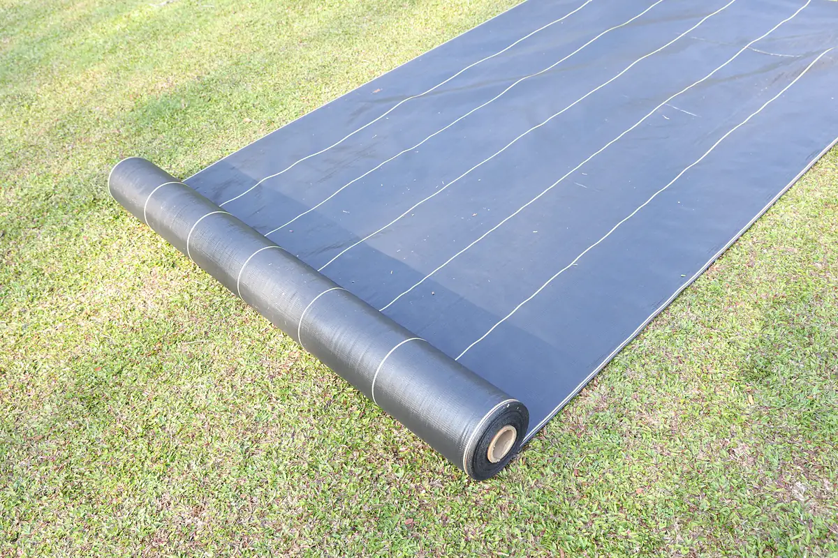SHIELD woven weed barrier unrolled on a lawn before bed planting