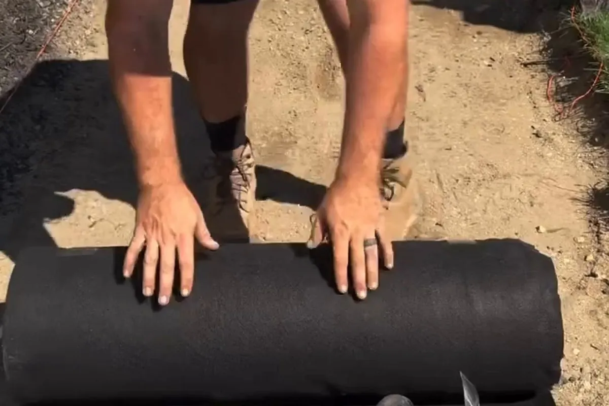 Hands on a roll of DOTDAY TERRA non-woven geotextile filter fabric at the start of an excavated path
