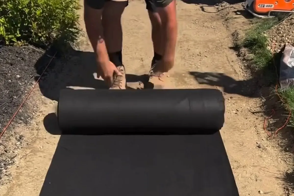 Installer unrolling black TERRA non-woven geotextile filter fabric into an excavated trench-style path