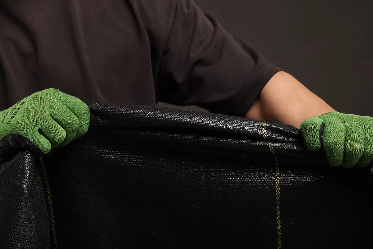 Gloved hands holding the dual-layer edge of XBAR 5 oz weed barrier fabric